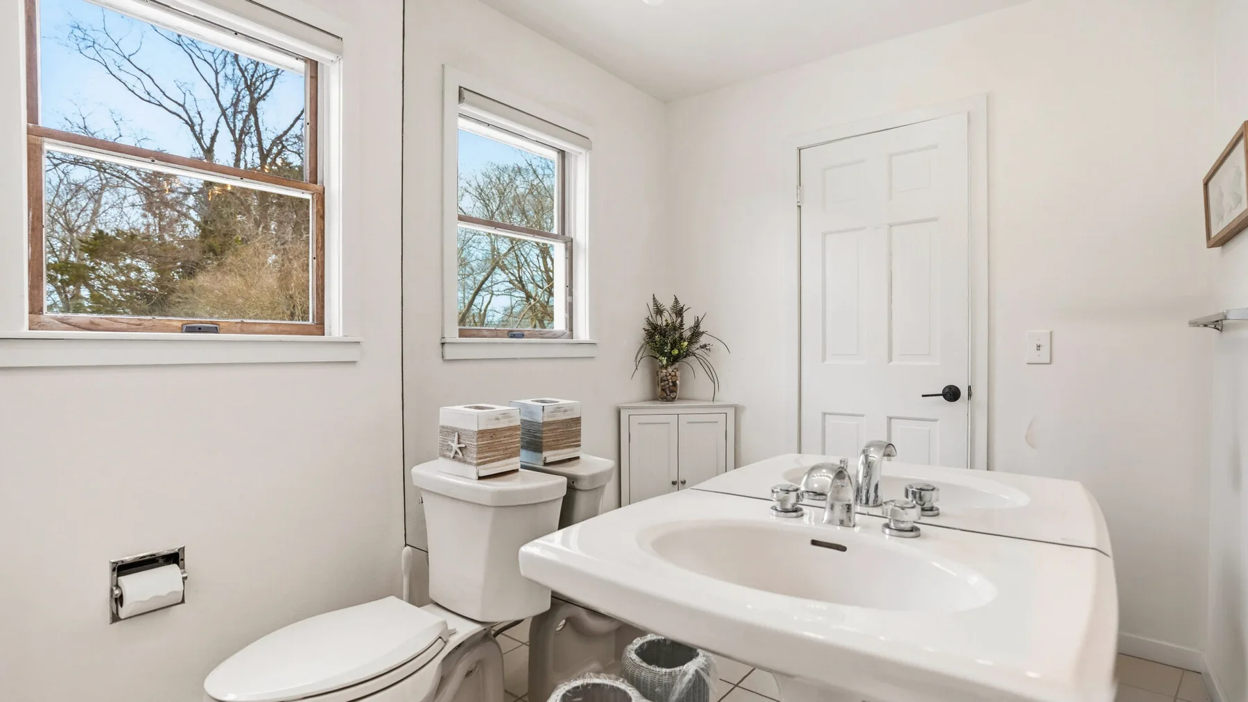 A bright bathroom with a wide sink, toilet, and windows.