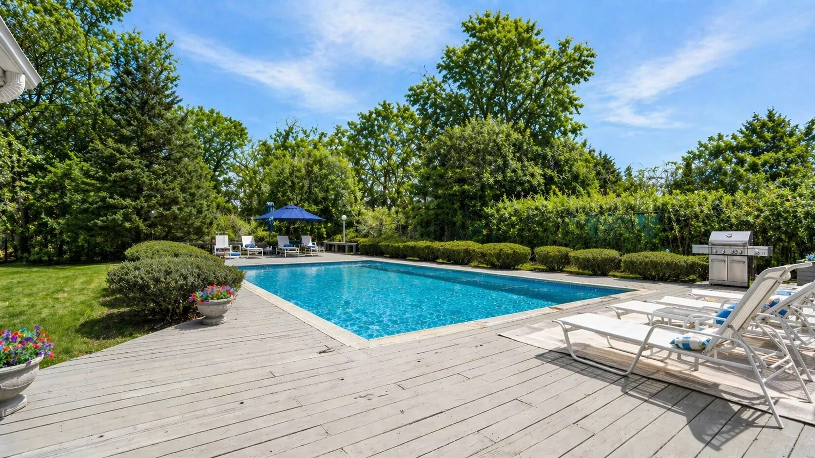 An outdoor swimming pool sits beside a spacious wooden deck and lounge seating.