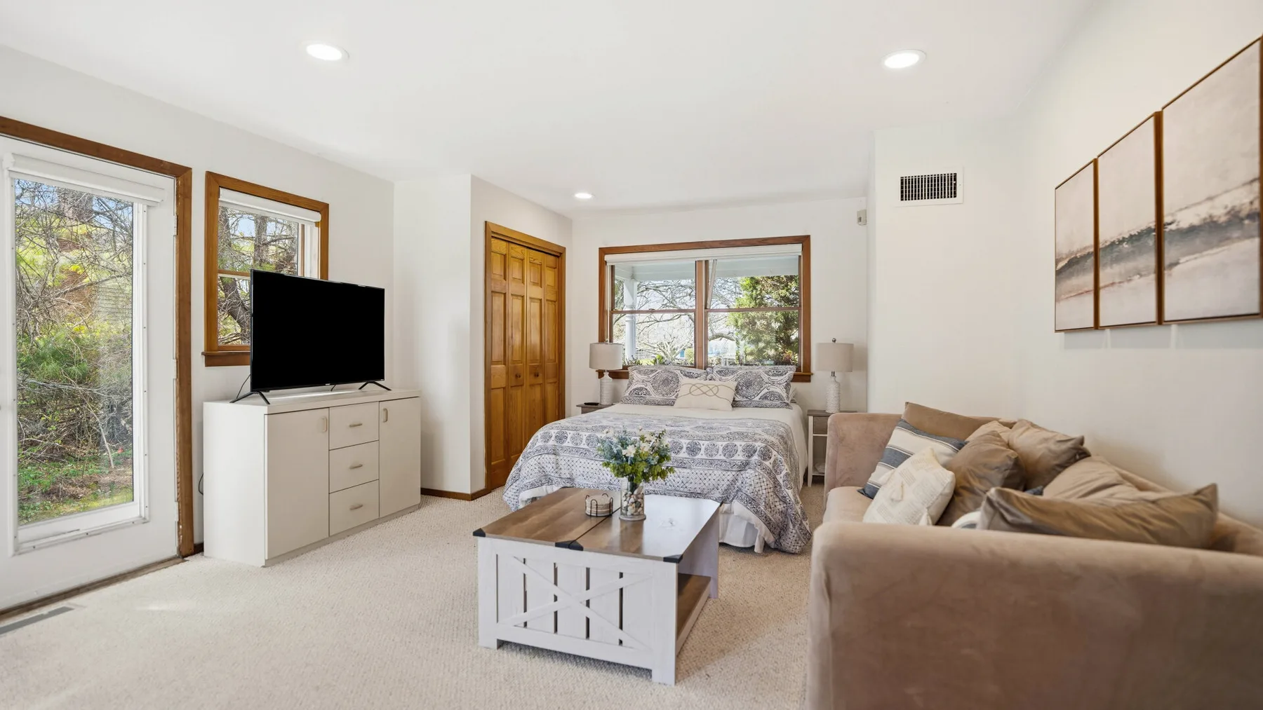 A bright bedroom with a bed, seating area, and television.