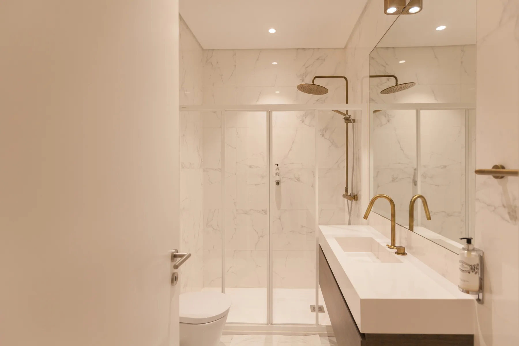 Un baño luminoso con una ducha de vidrio y un largo lavabo.
