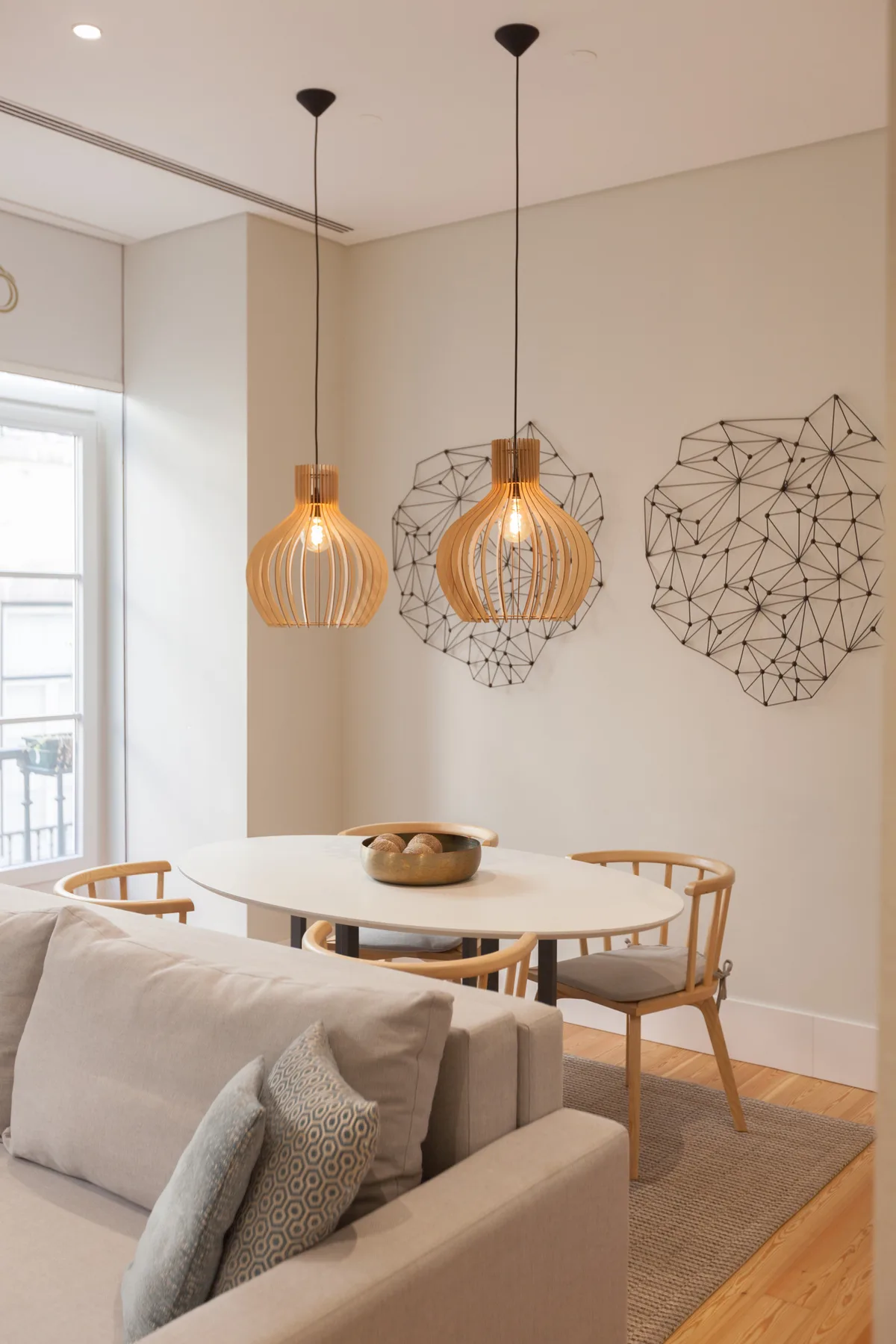 Un comedor con una mesa redonda, lámparas colgantes y adornos geométricos en la pared.