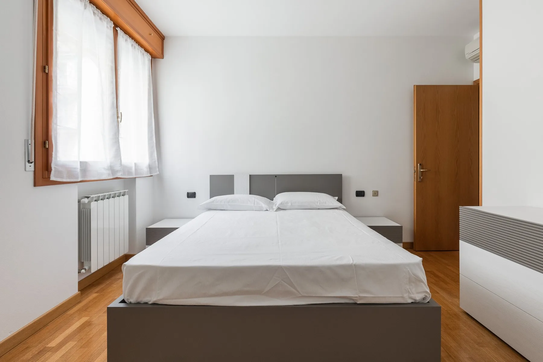 Un dormitorio con una cama centrada entre dos mesitas de noche.