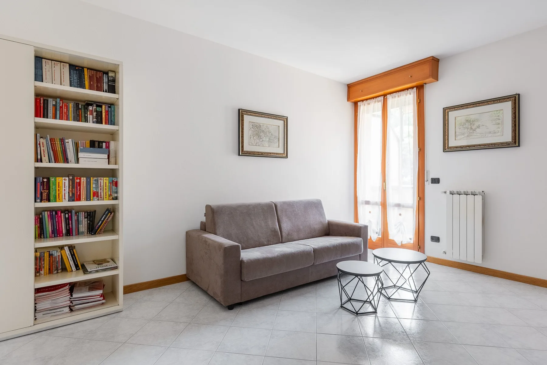 Una sala de estar con un sofá, dos mesitas y una librería alta.