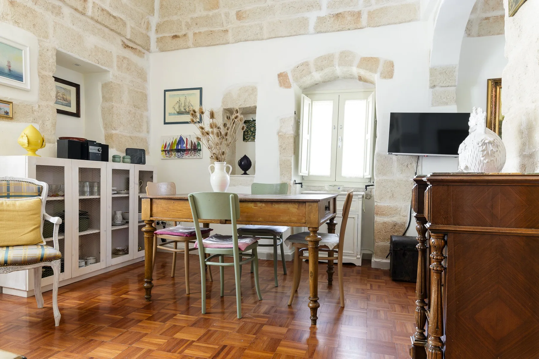 Comedor con paredes de piedra, una mesa de madera, sillas y un televisor.