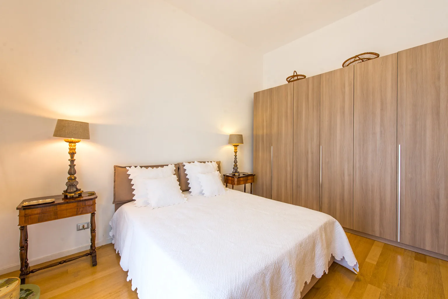 Un dormitorio con una cama blanca, mesitas de noche y un armario grande.