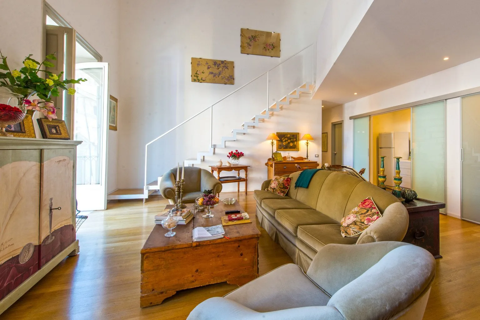 A bright living room with seating, a coffee table, and a staircase.