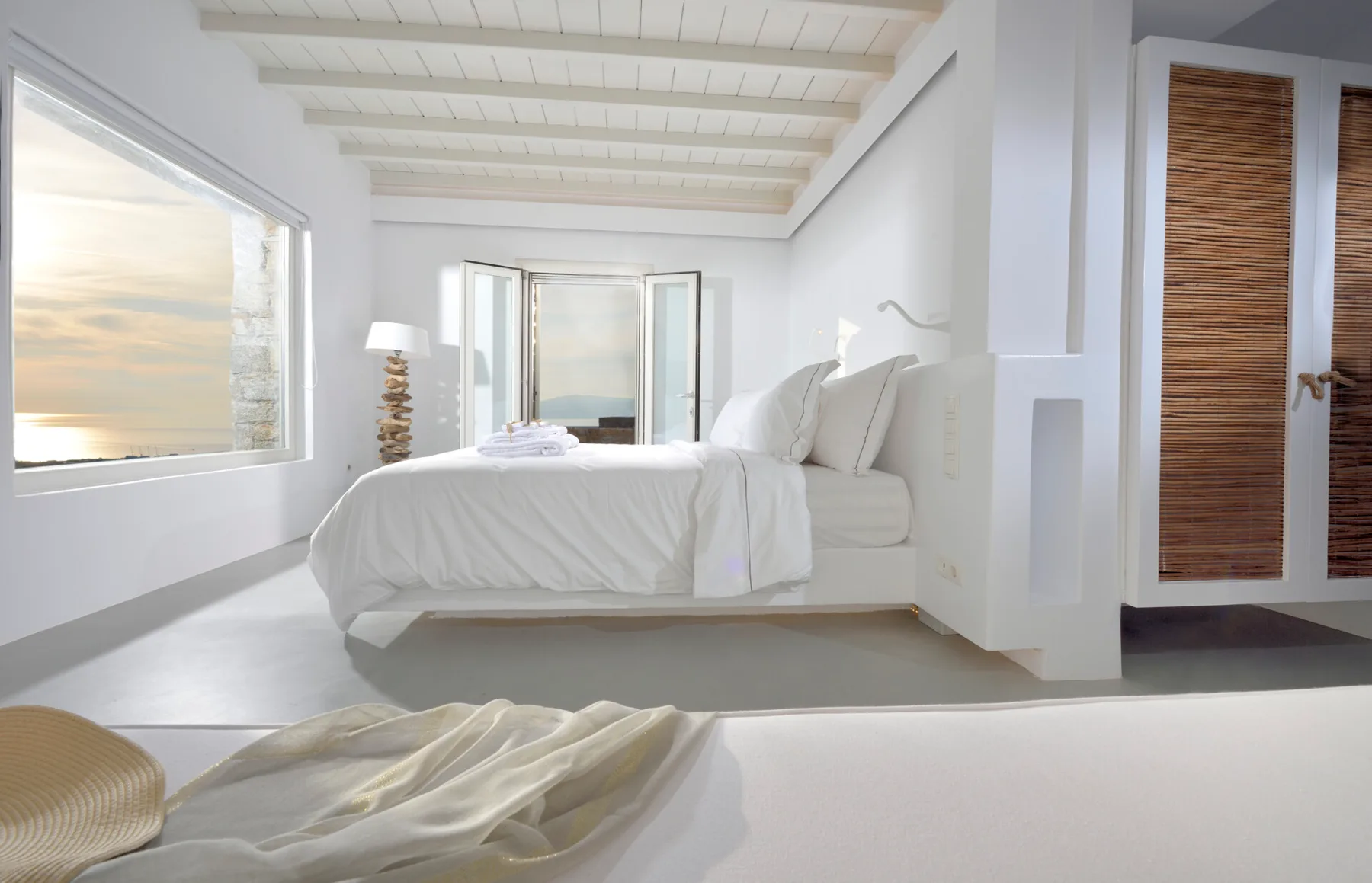 A bright bedroom with a white bed beside large windows.