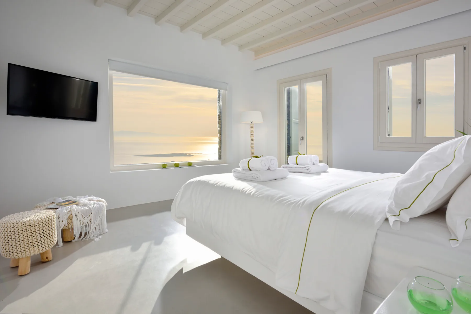 A bright bedroom with white bedding and a large window overlooking the water.