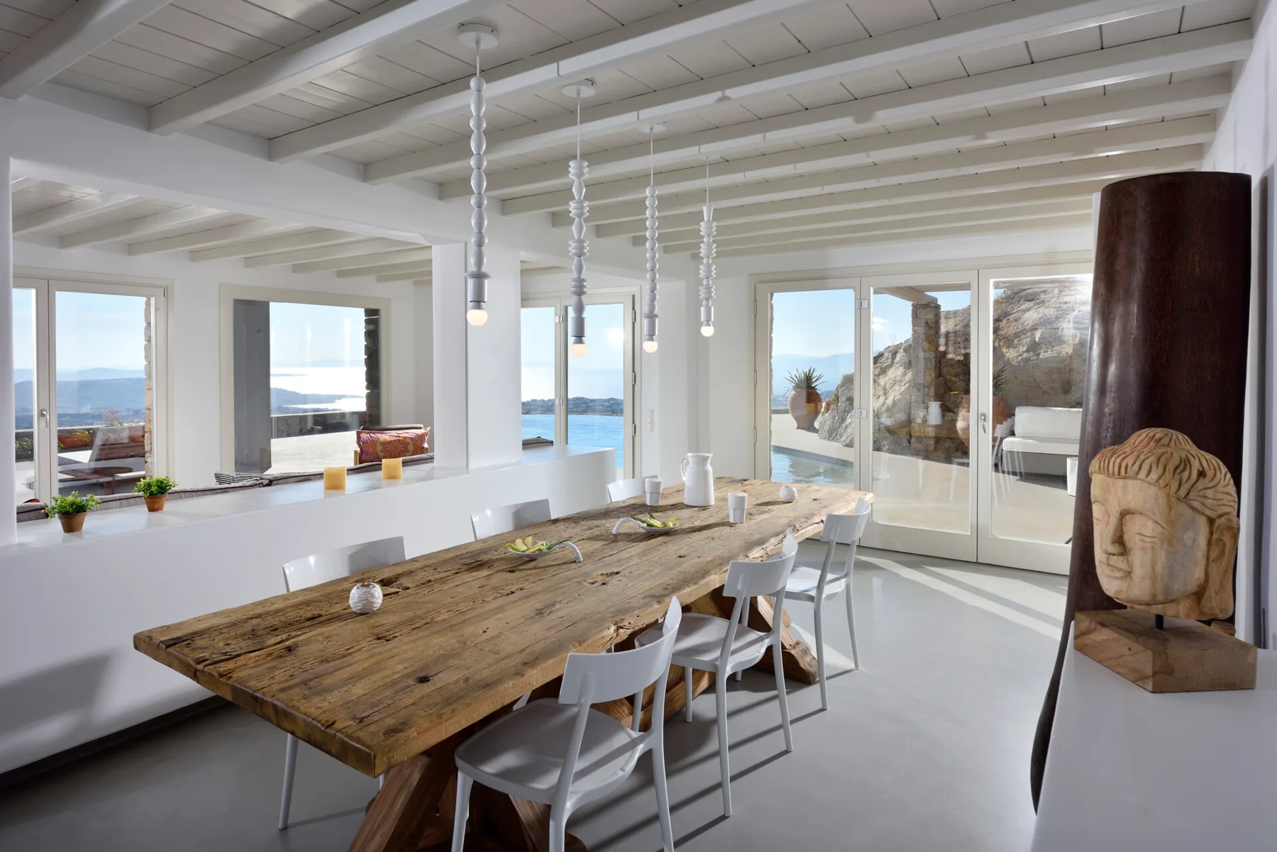 A bright dining area with a long wooden table and views of the sea.