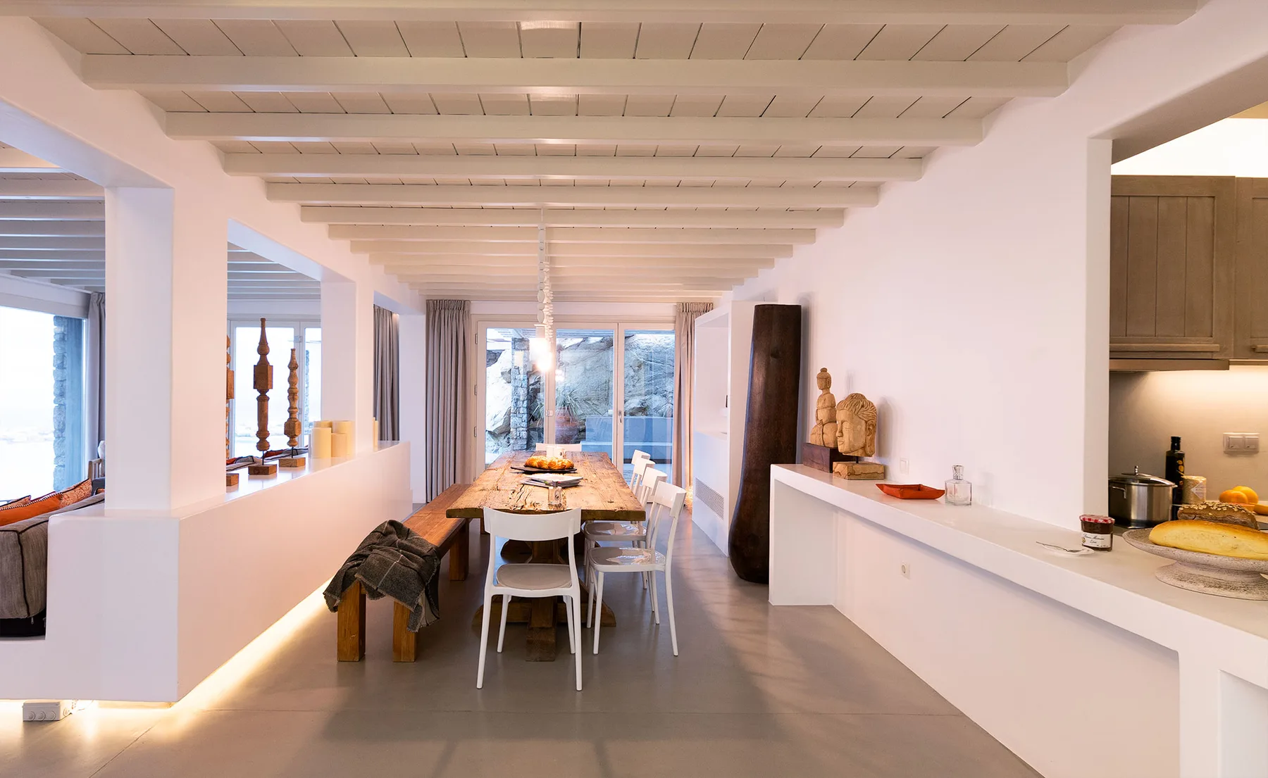 A bright open-plan dining area with a long table and a kitchen counter.