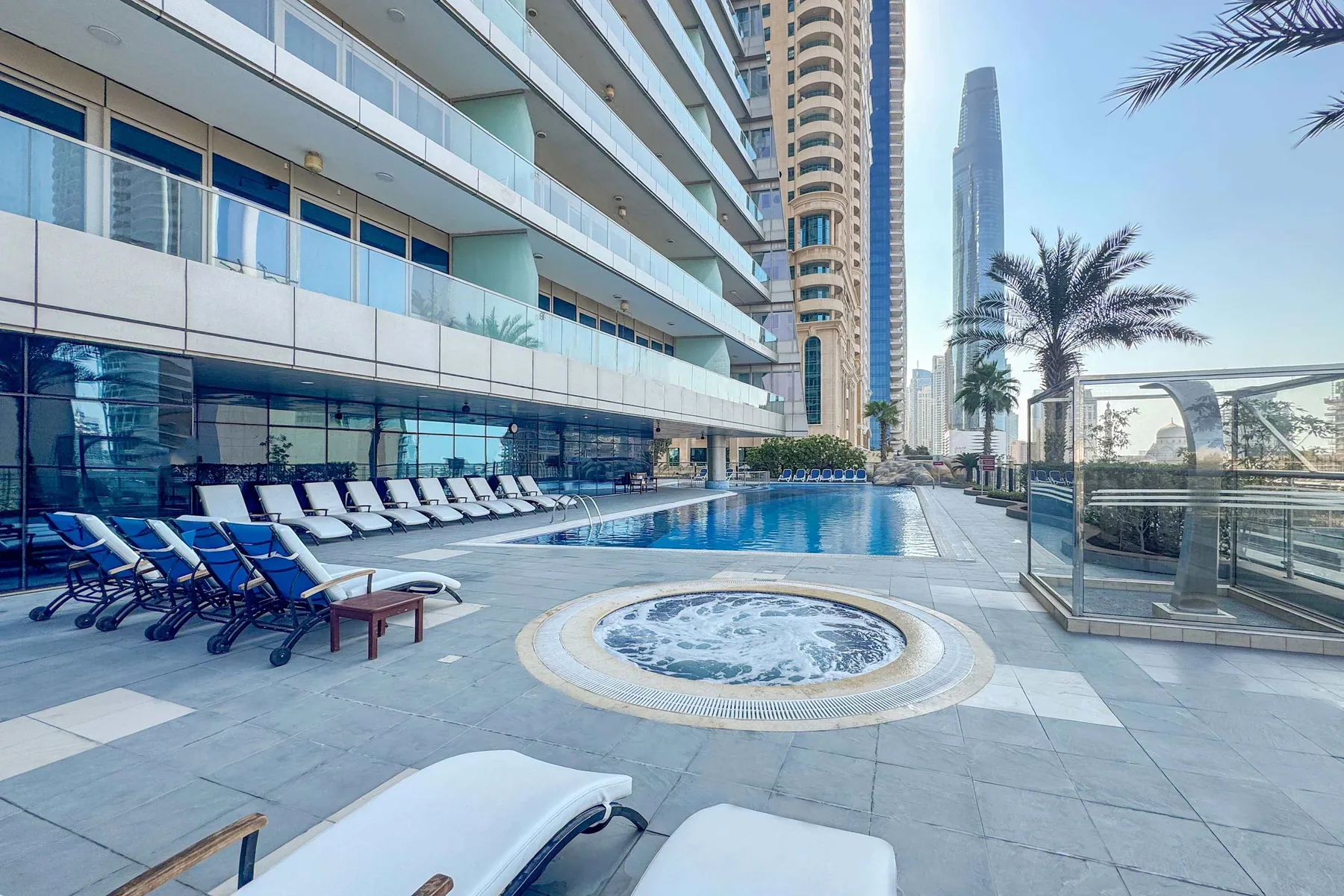An outdoor pool deck with lounge seating and a circular spa.