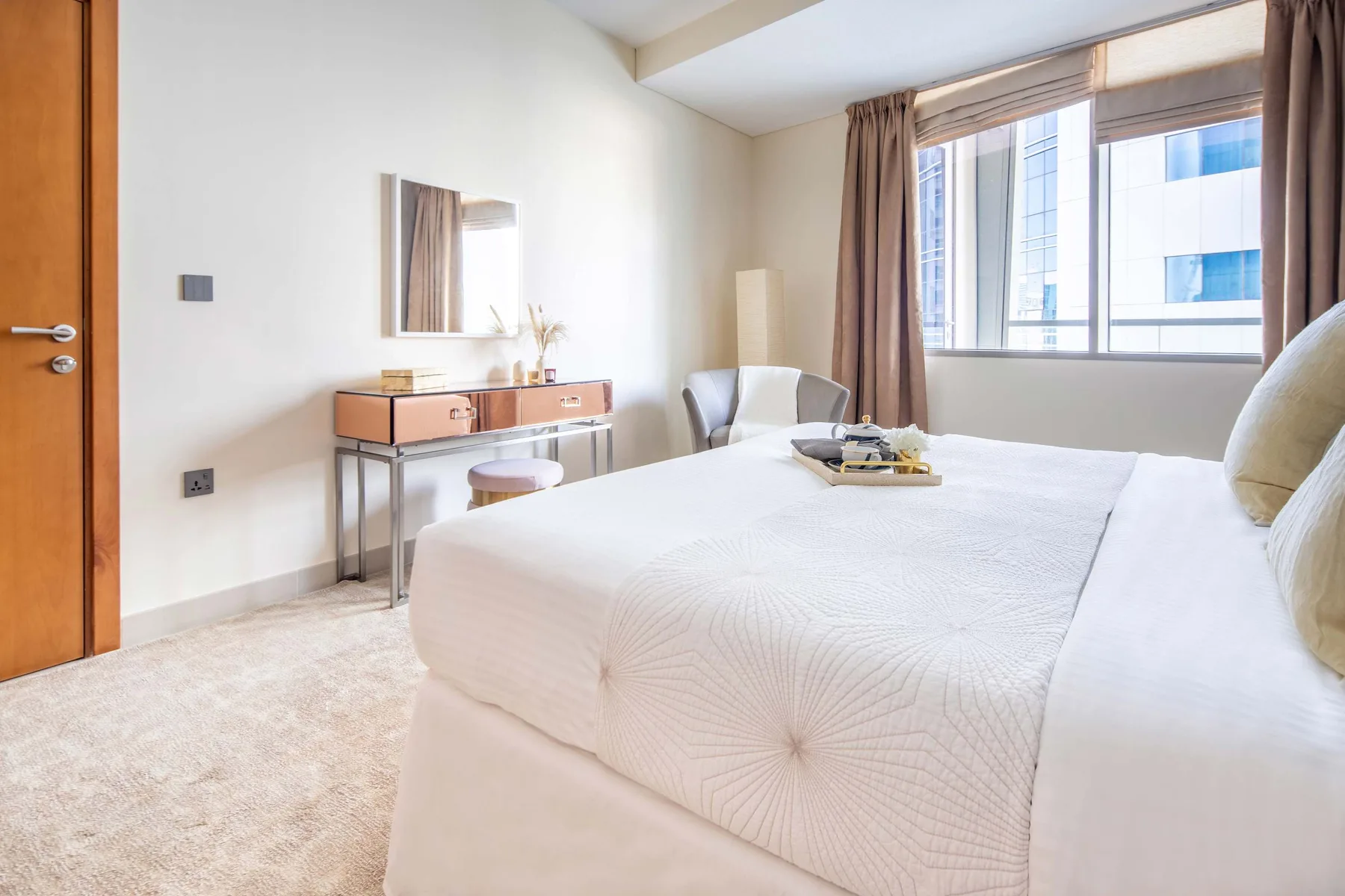 A bright bedroom with a neatly made bed and a desk beside the window.