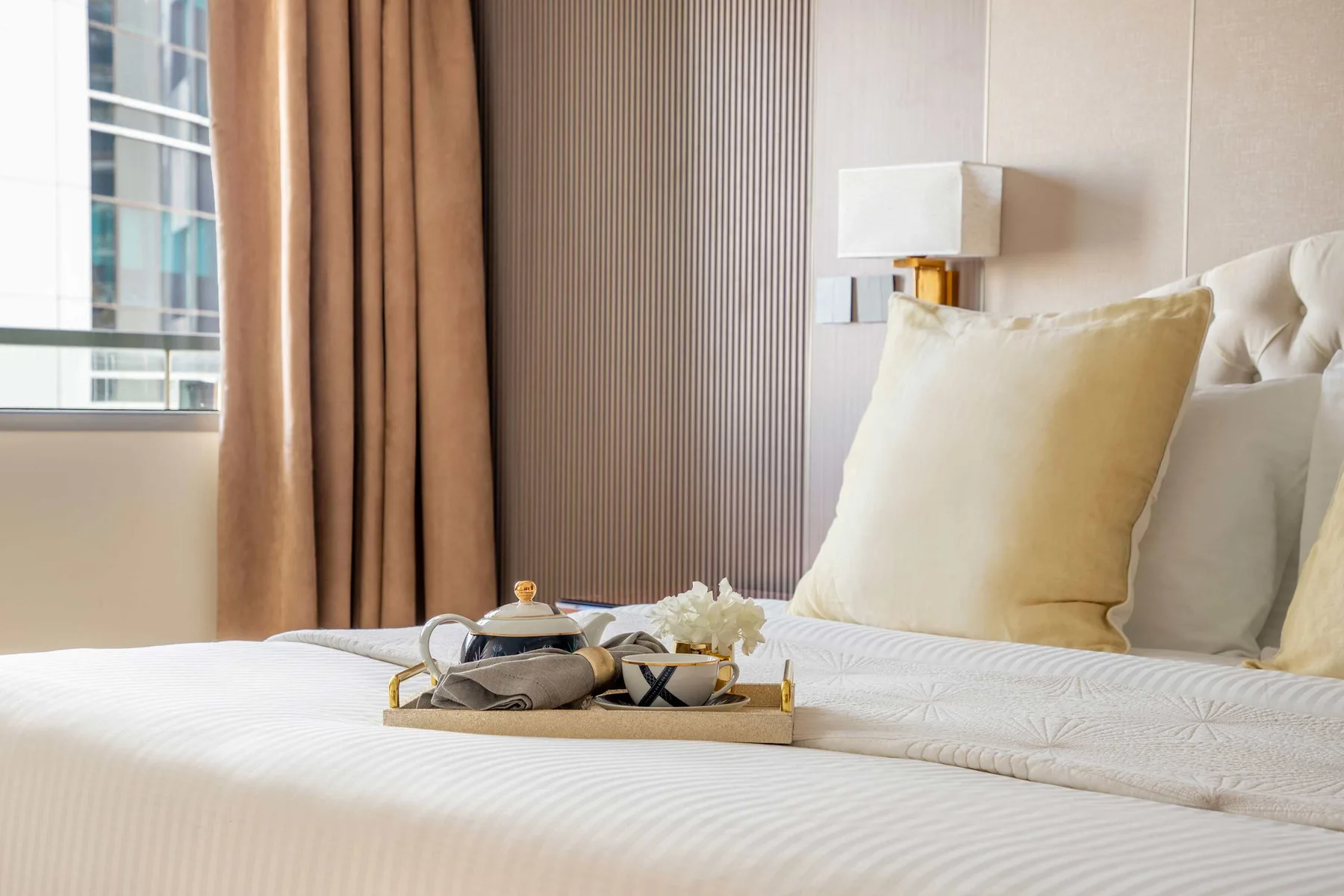 A neatly made bedroom bed sits beside a window with brown curtains.