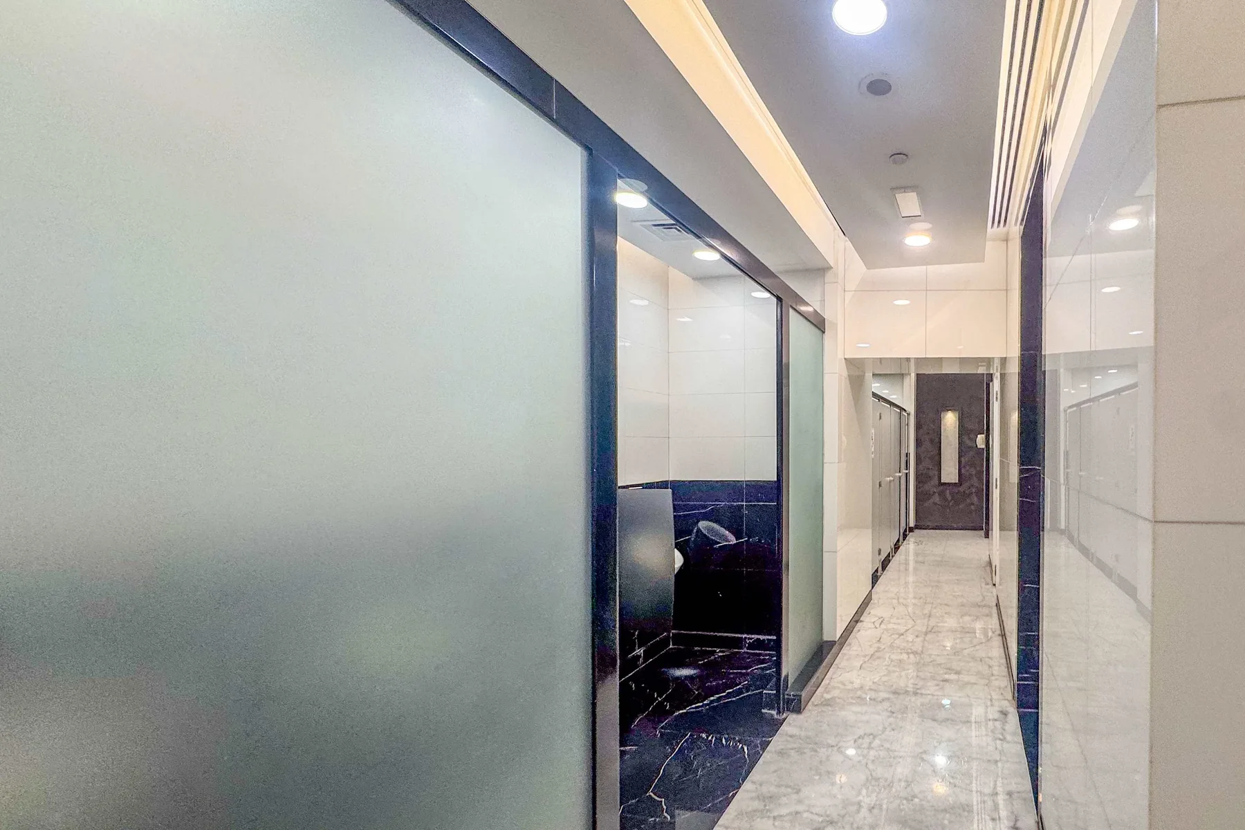 A tiled hallway with glass partitions and a dark doorway at the far end.