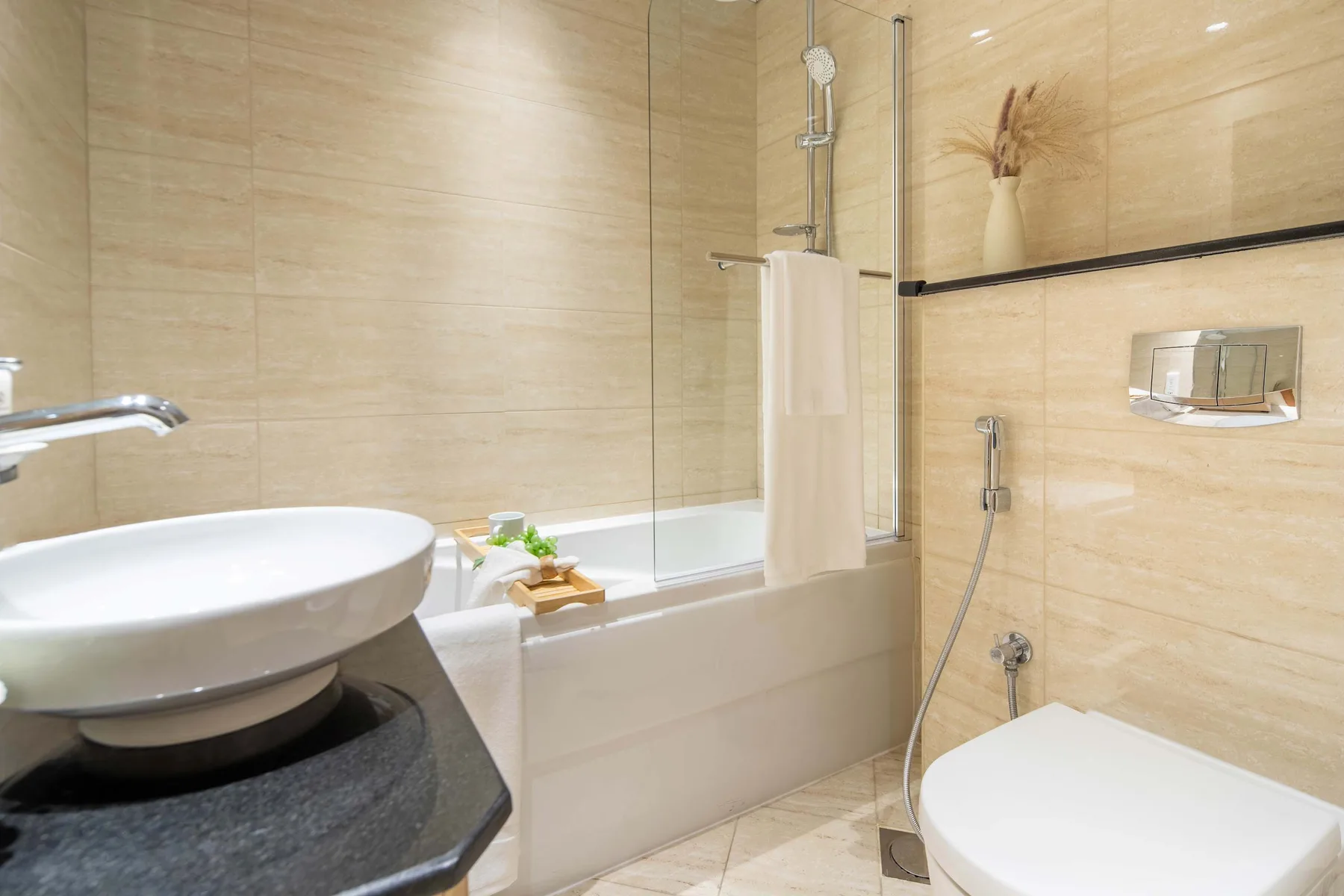 A tiled bathroom with a bathtub, glass shower screen, sink, and toilet.