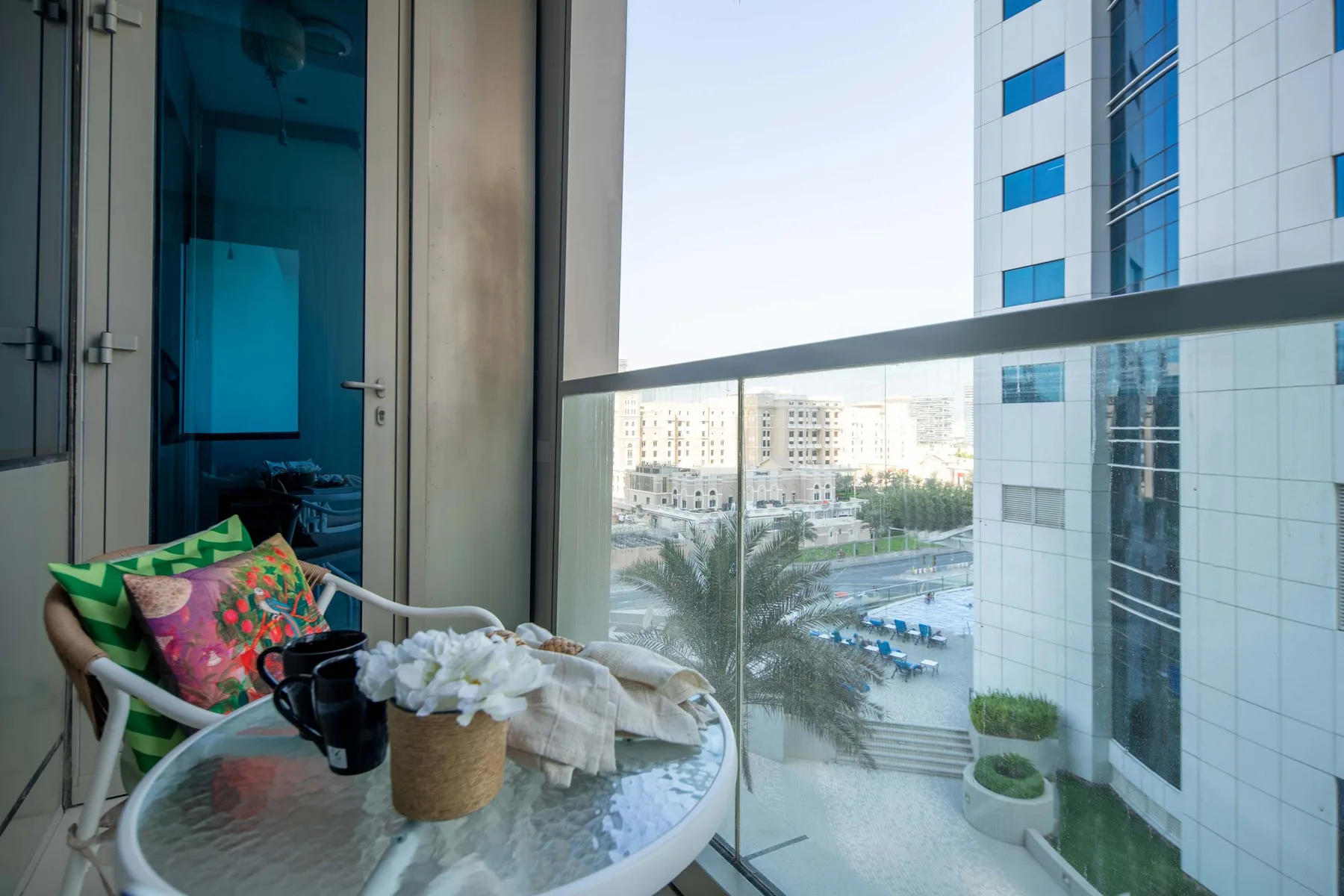 A small seating area beside a glass balcony overlooks nearby buildings.