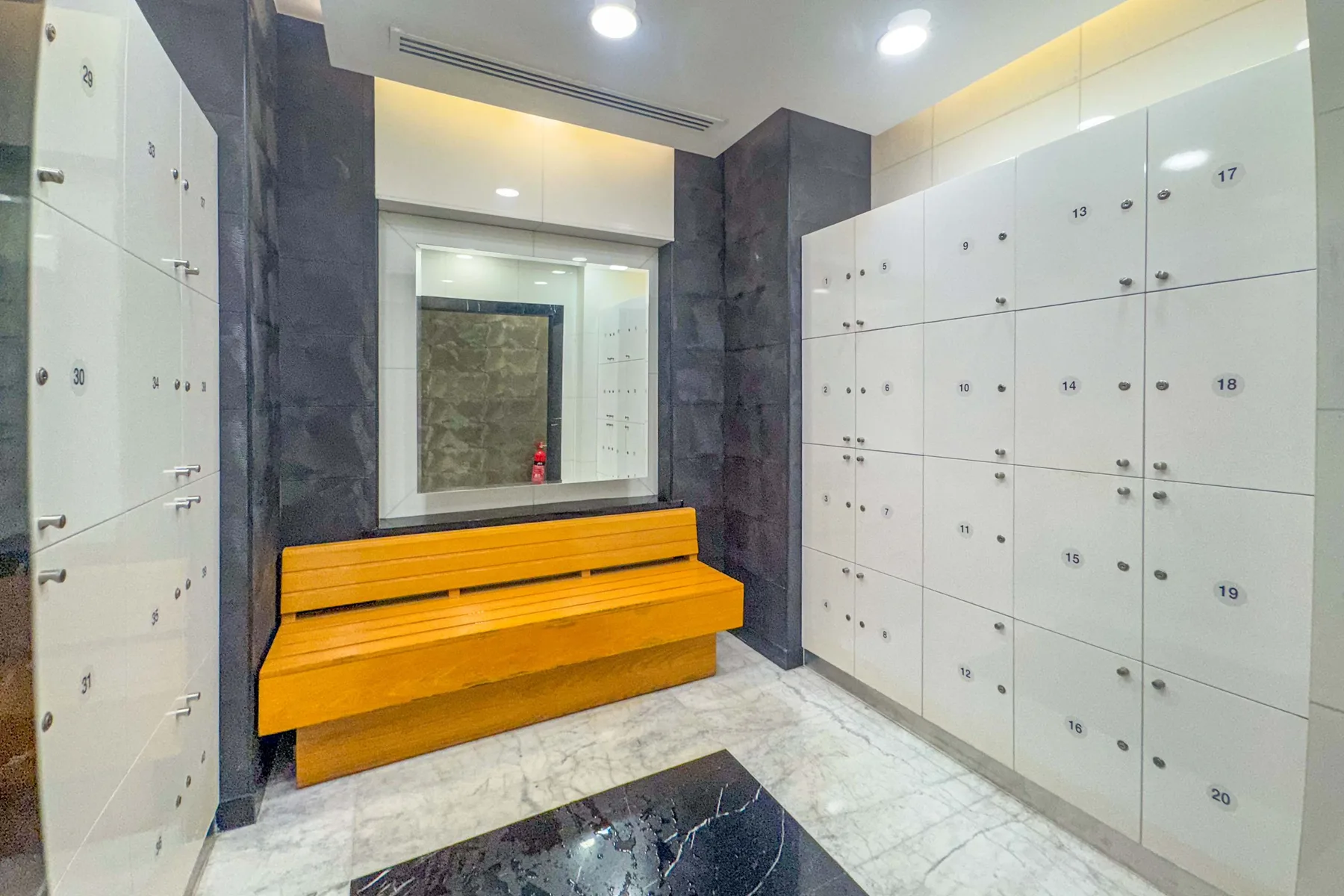 A locker room with white storage lockers and a wooden bench.