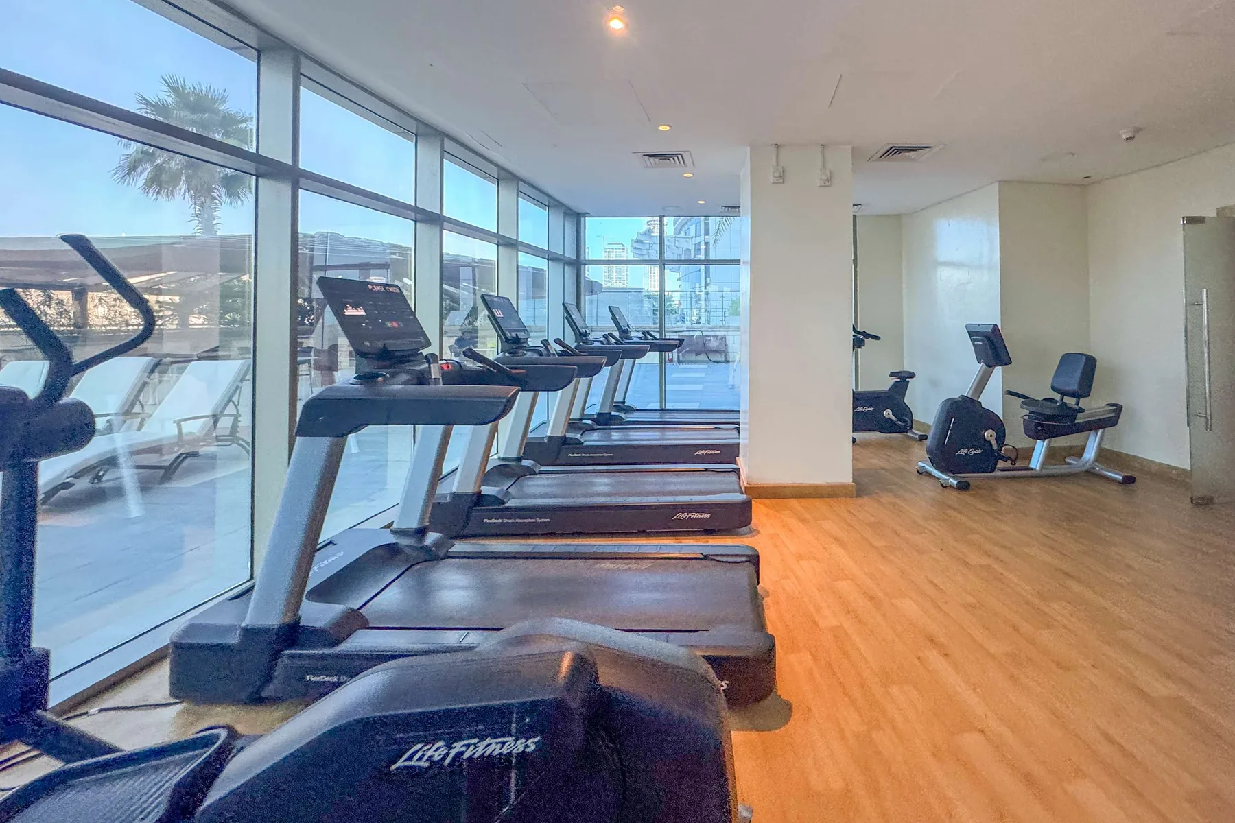 A gym with treadmills and exercise bikes beside large windows.