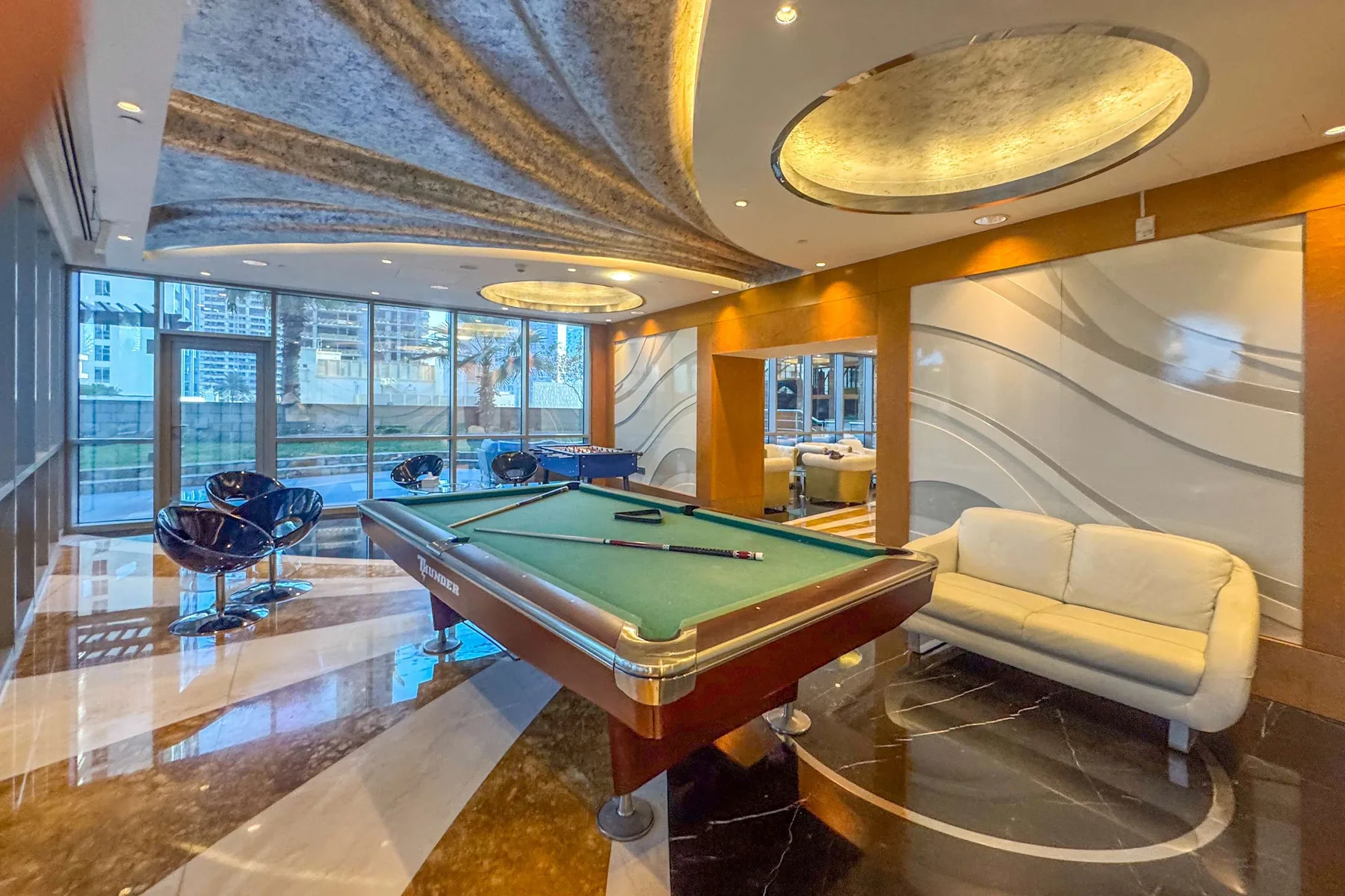 A billiards room with a pool table, lounge seating, and large windows.