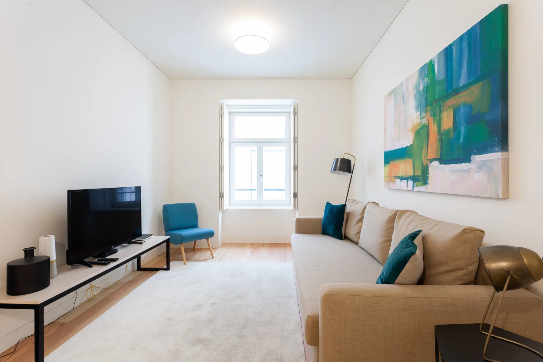 Sala de estar con sofá beige, televisor y arte colorido en la pared.