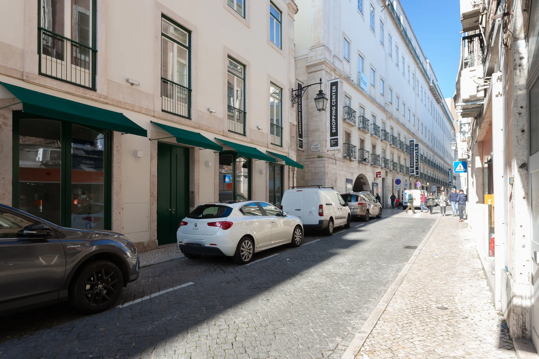 Una calle estrecha de ciudad flanqueada por edificios altos y vehículos estacionados.
