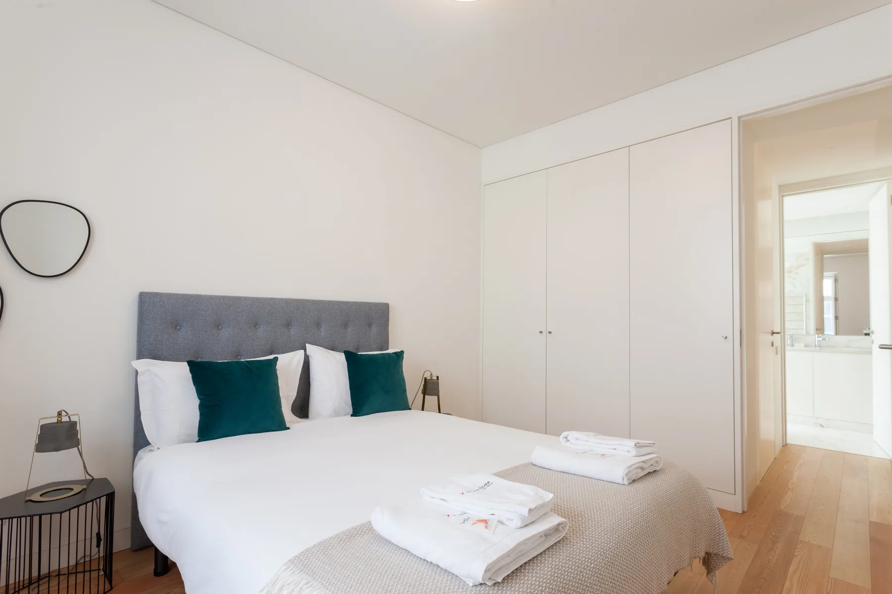 Un dormitorio luminoso con cama, almohadas verde azulado y armarios empotrados blancos.