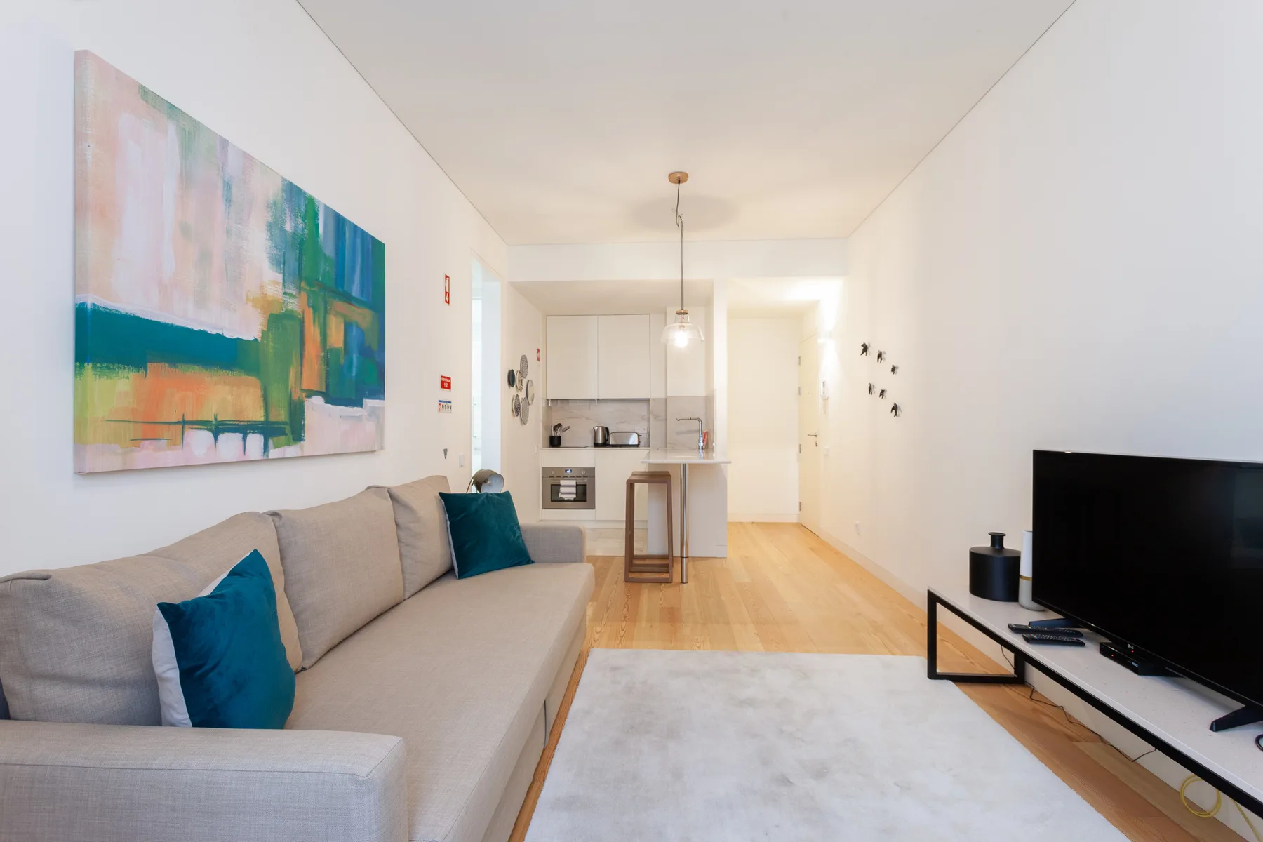 Una sala luminosa con asientos, un televisor y una cocina abierta.