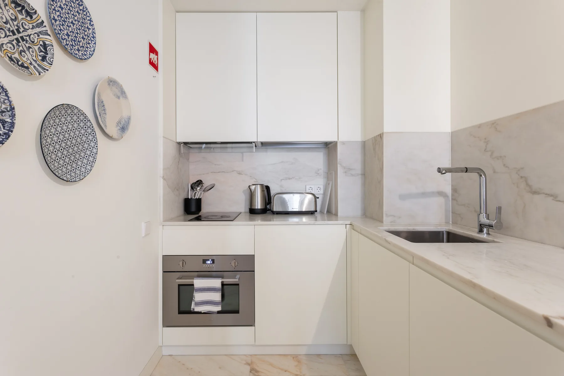 Una cocina compacta con armarios blancos, una encimera y un fregadero.