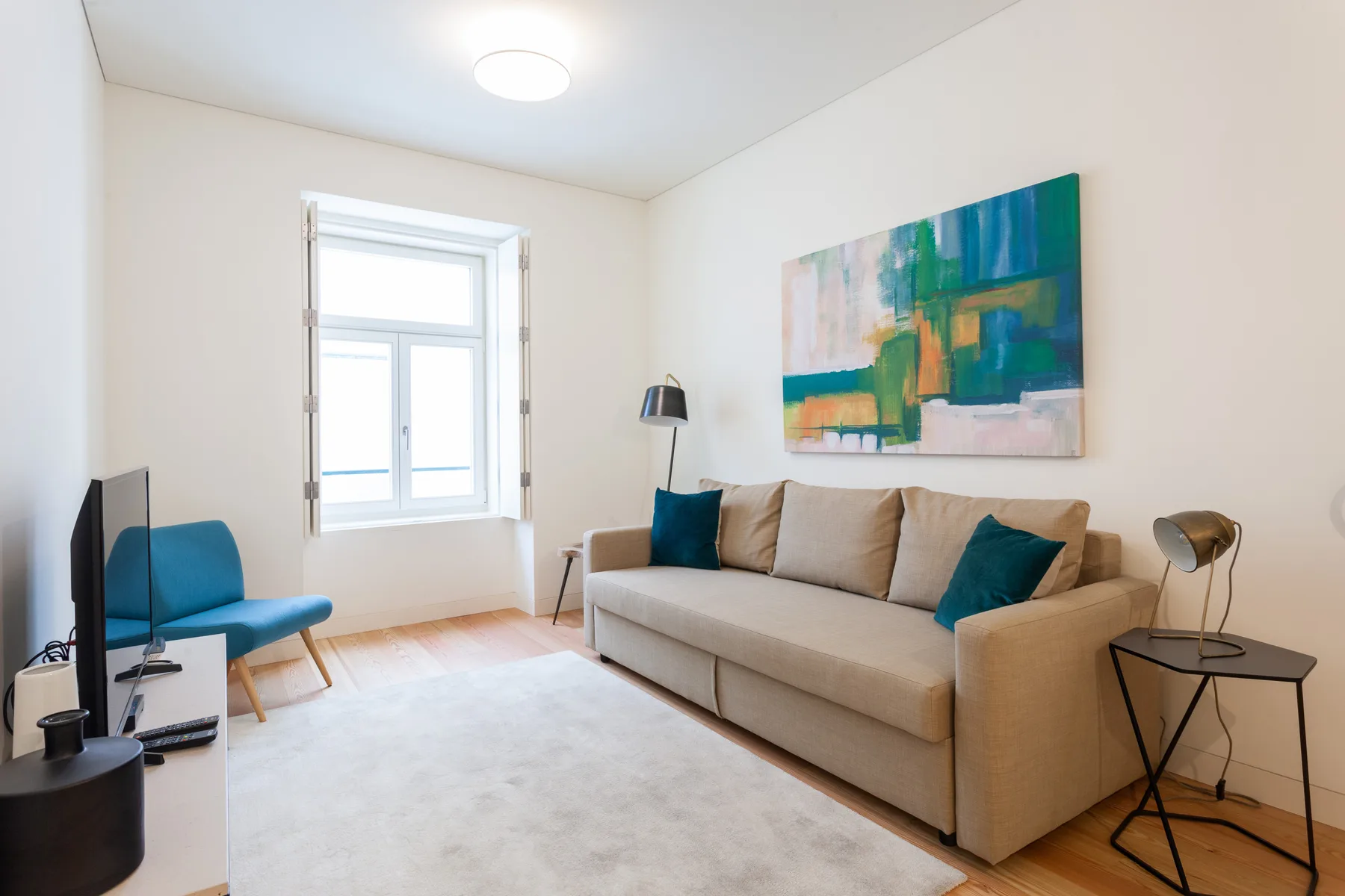 Sala de estar con asientos beige, una ventana y arte colorido en la pared.