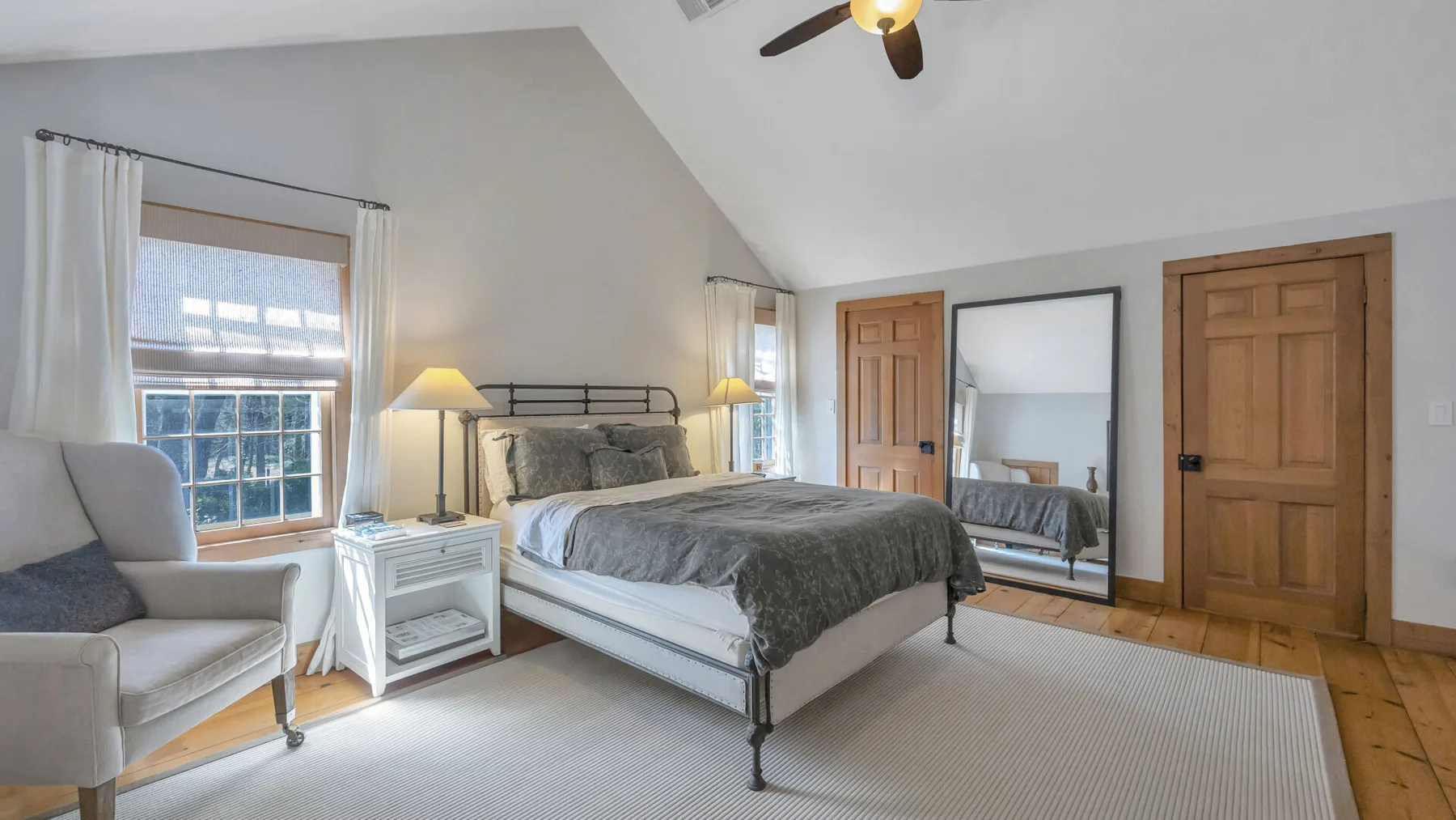 Un dormitorio con una cama, un sillón y ventanas con cortinas.