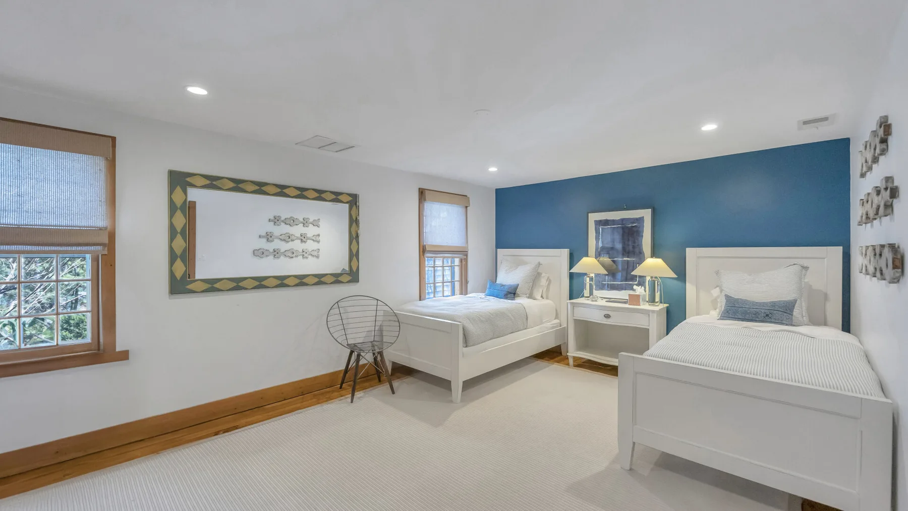 Un dormitorio luminoso con dos camas blancas frente a una pared azul.