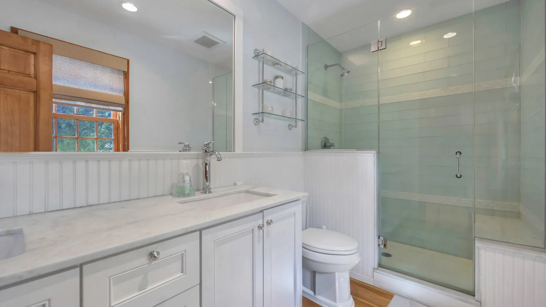 Un baño luminoso con un lavabo largo, un inodoro y una ducha de vidrio.
