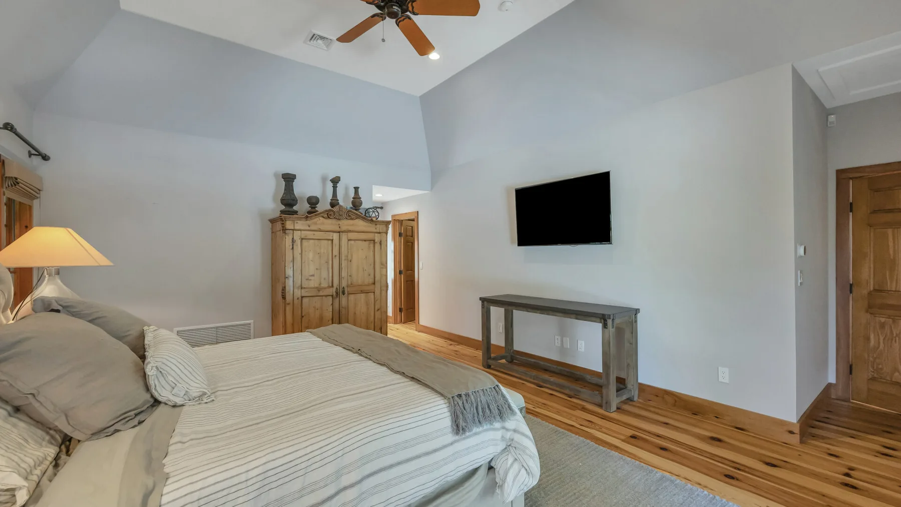 Un dormitorio con una cama, un armario de madera y un televisor en la pared.