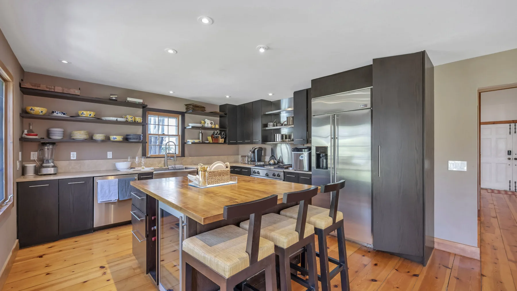 Una cocina amplia con isla de madera, estantes abiertos y electrodomésticos de acero inoxidable.