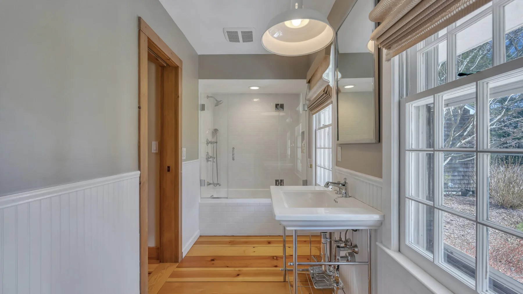 Un baño luminoso con ducha de vidrio, lavabo y ventanas grandes.