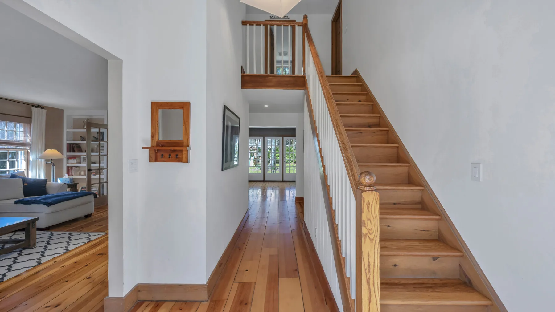 Un pasillo luminoso con una escalera de madera y suelo de madera pulida.