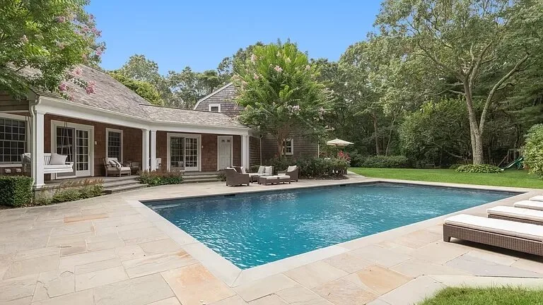 Una piscina y un patio pavimentado están junto a una casa y un jardín.
