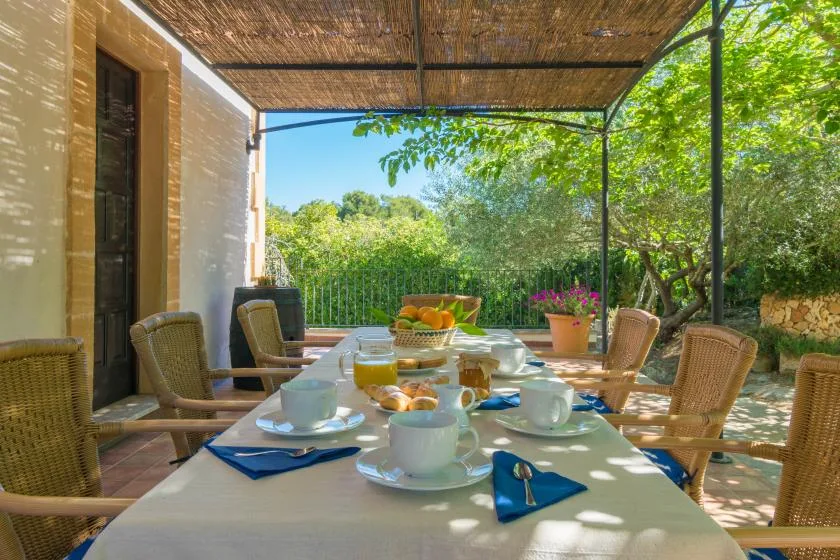Comedor al aire libre con una mesa puesta bajo un toldo de sombra.