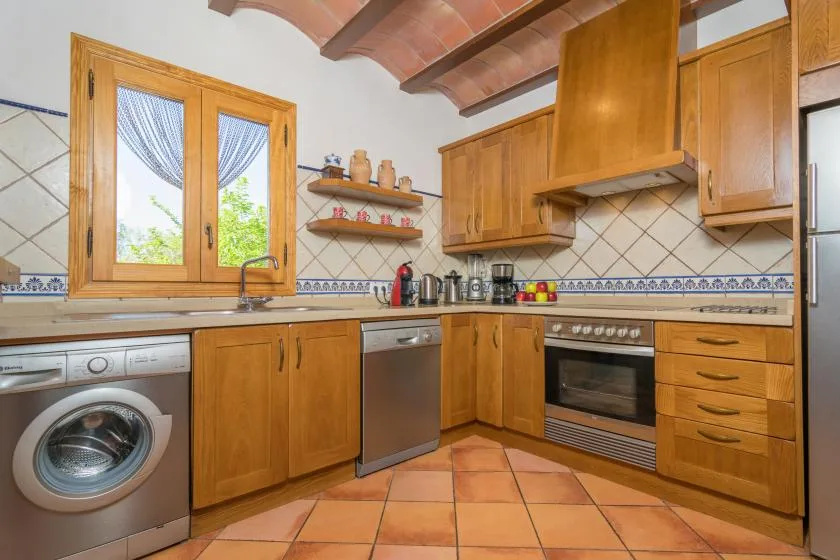 Una cocina con armarios de madera, suelo de baldosas y una ventana sobre el fregadero.