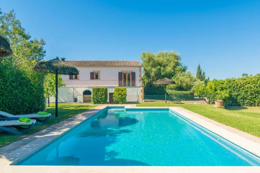 Una piscina junto a una casa de dos plantas, con árboles y setos alrededor del jardín.