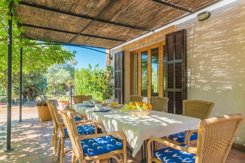Un comedor exterior sombreado con una mesa larga junto a la casa.