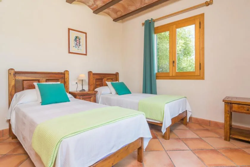 Un dormitorio con dos camas, almohadas turquesas y una ventana con vistas a la vegetación.