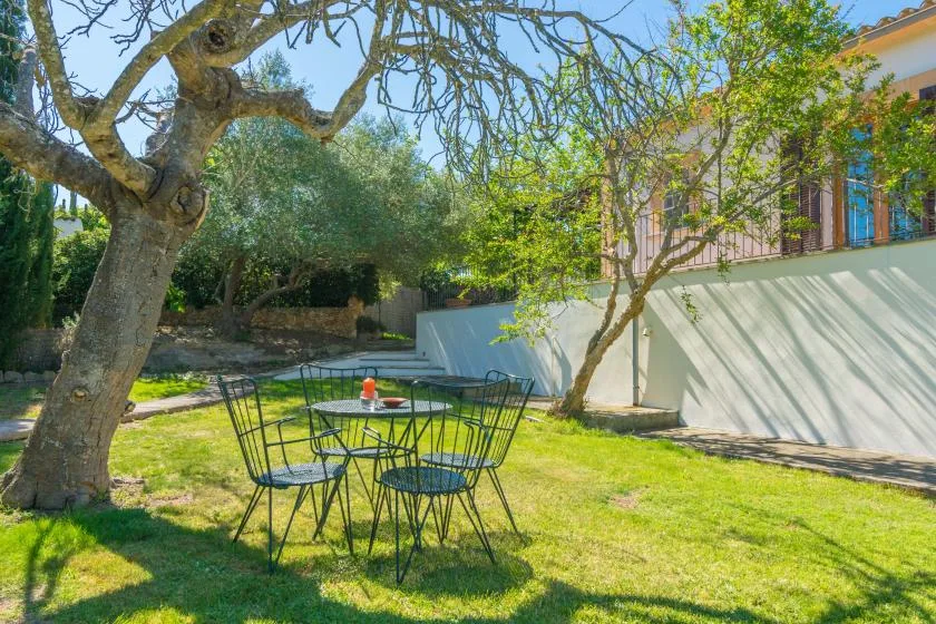 Una zona de asientos en el jardín con una mesa y sillas de metal bajo árboles frondosos.