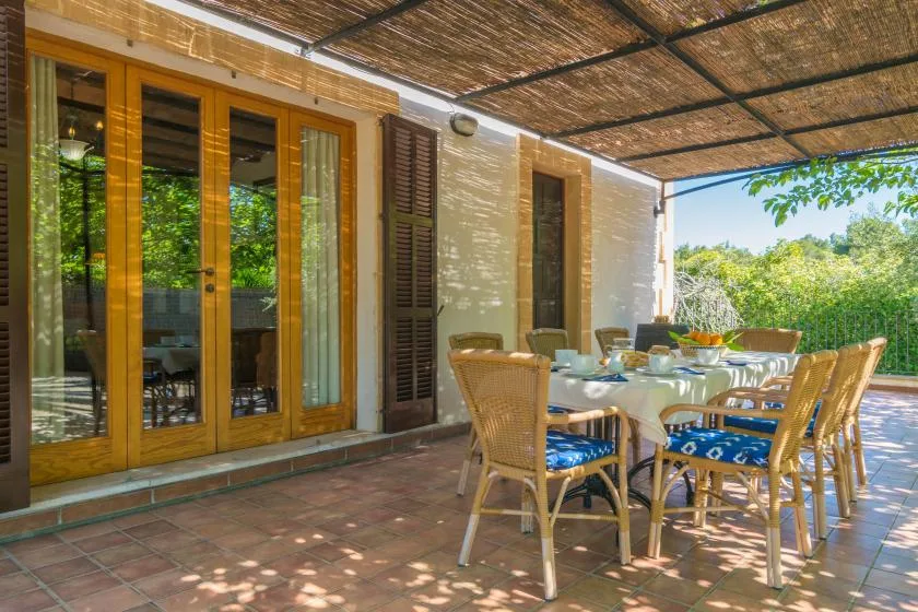 Un comedor exterior cubierto con una mesa y asientos de mimbre junto a puertas de vidrio.