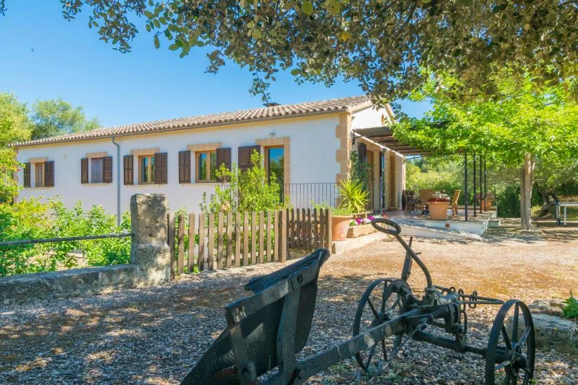 Una casa blanca con ventanas de persianas y una zona de estar al aire libre a la sombra.
