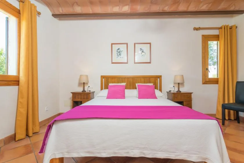 Un dormitorio con una cama vestida de blanco y rosa intenso, entre dos ventanas.