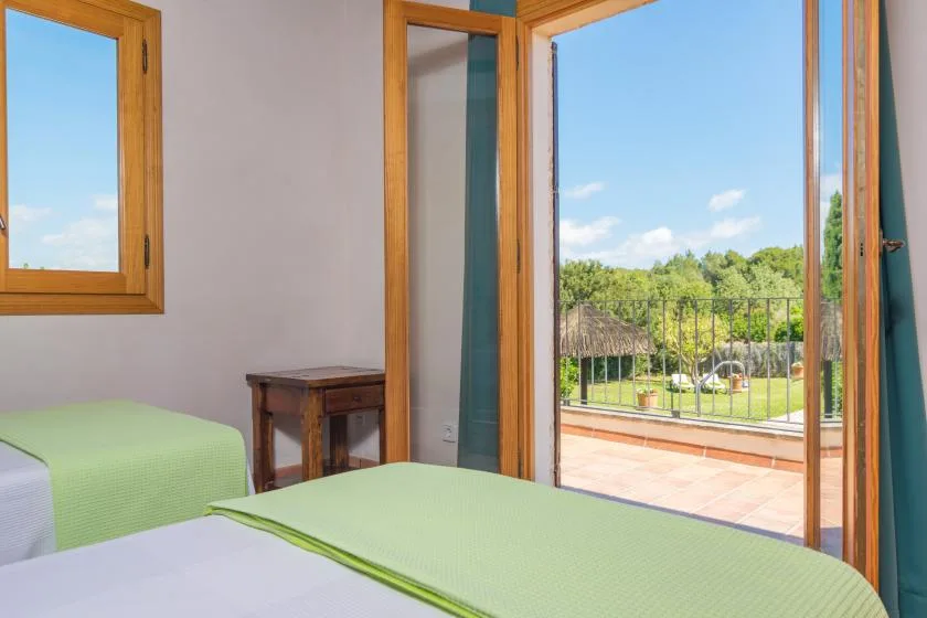 Un dormitorio con camas cubiertas de verde junto a puertas abiertas que dan a un jardín.