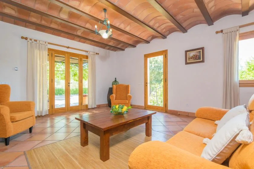 Una sala luminosa con asientos naranjas, una mesa de centro de madera y puertas de vidrio.