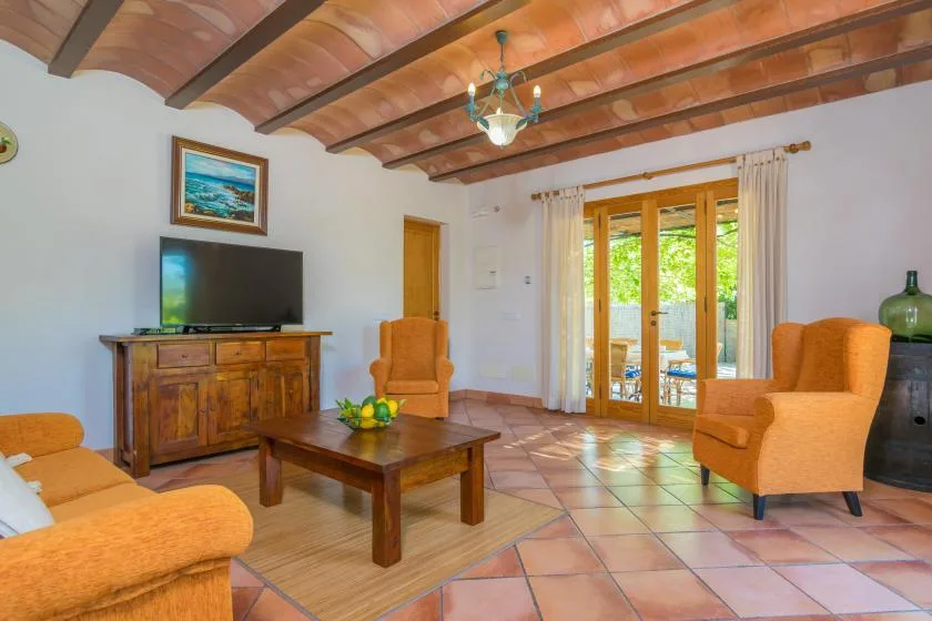 Una sala de estar con asientos naranjas, una mesa de centro de madera y puertas de vidrio hacia un patio.