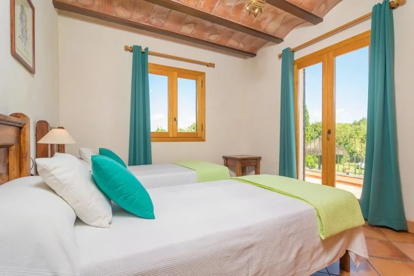Un dormitorio con dos camas vestidas de blanco y verde junto a una puerta acristalada.